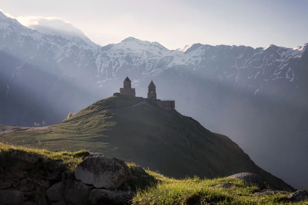 Gergeti Trinity Church on its green hill in evening light, snowy peaks behind