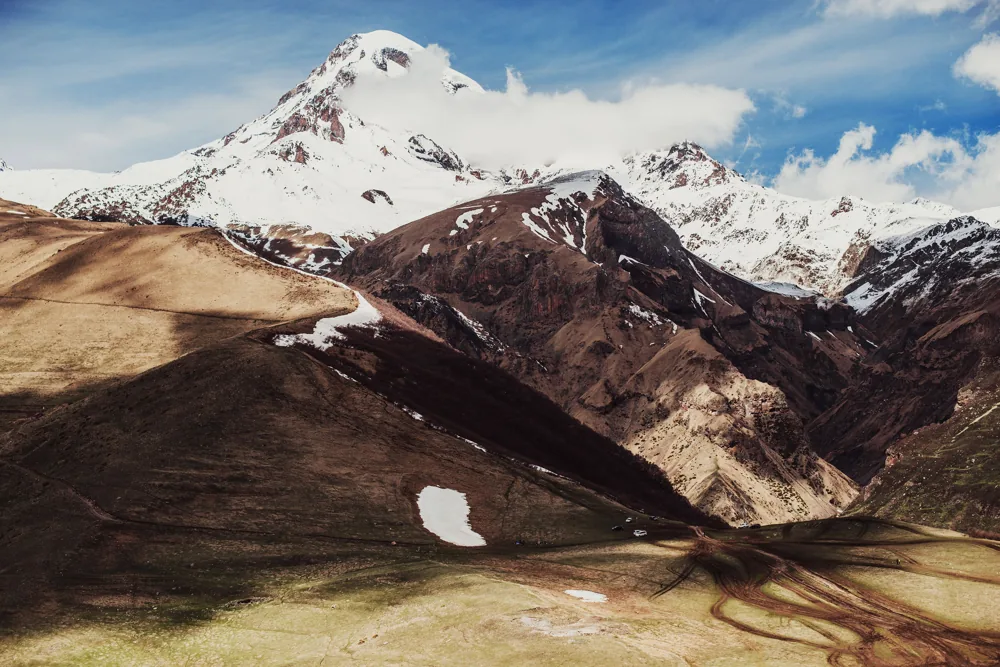 Snow on Mount Kazbek above brown ridges and green pasture under a blue sky