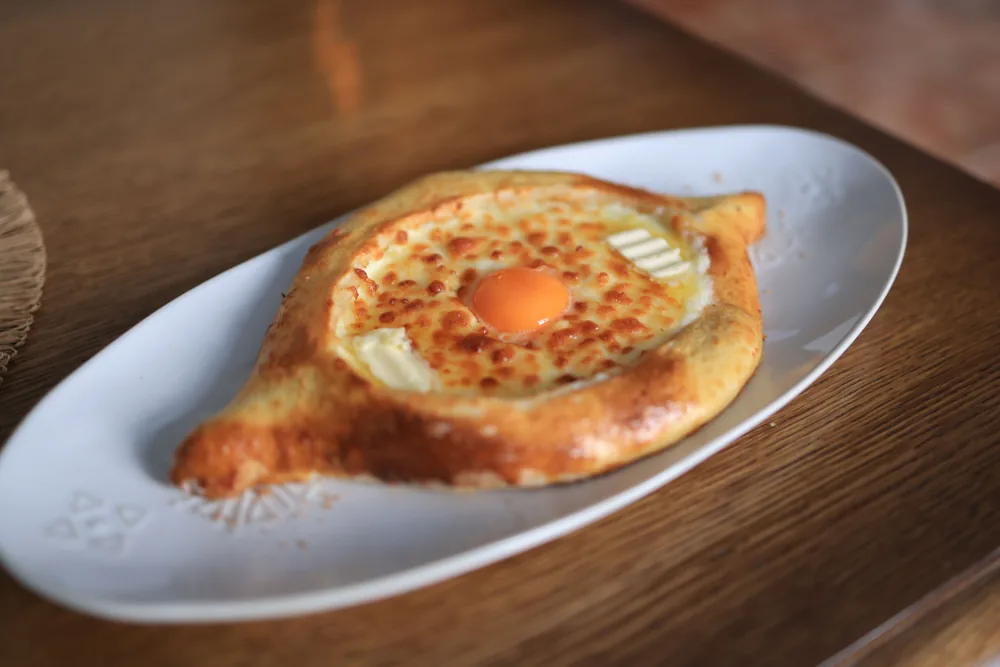 An Adjarian khachapuri boat with melted cheese, butter and a bright egg yolk on a white oval plate