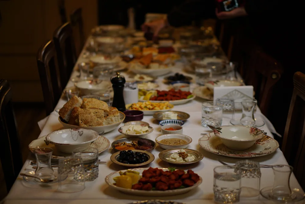 A long table under a white cloth, crowded with bread, cheese, olives, sausages and cut-glass tumblers