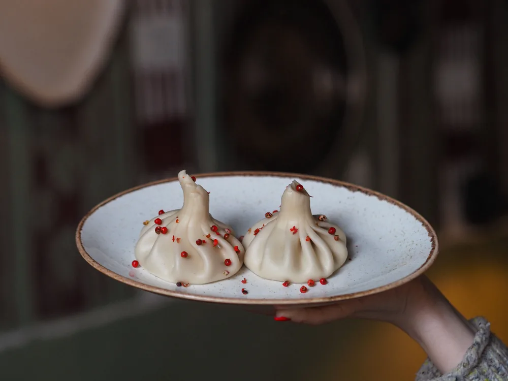 A hand holding out a plate with two khinkali sprinkled with pink peppercorns