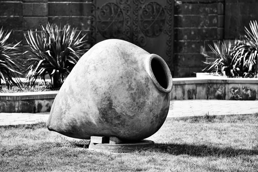 A large clay vessel lying on its side on the grass in black and white, its rolled rim open to the camera